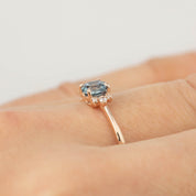 Close-up of a 14k rose gold ring with a 0.72ct blue Montana sapphire and small diamonds on a finger.