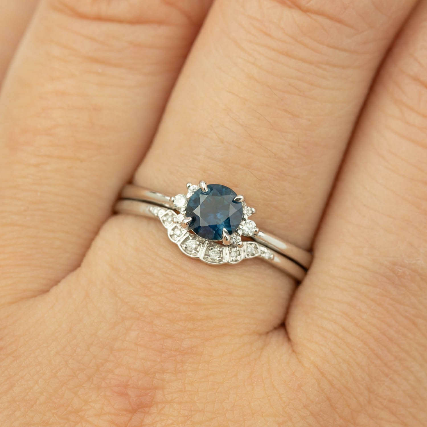 Close-up of a 0.65ct blue Montana sapphire ring and diamond band in recycled 14k white gold on a finger.