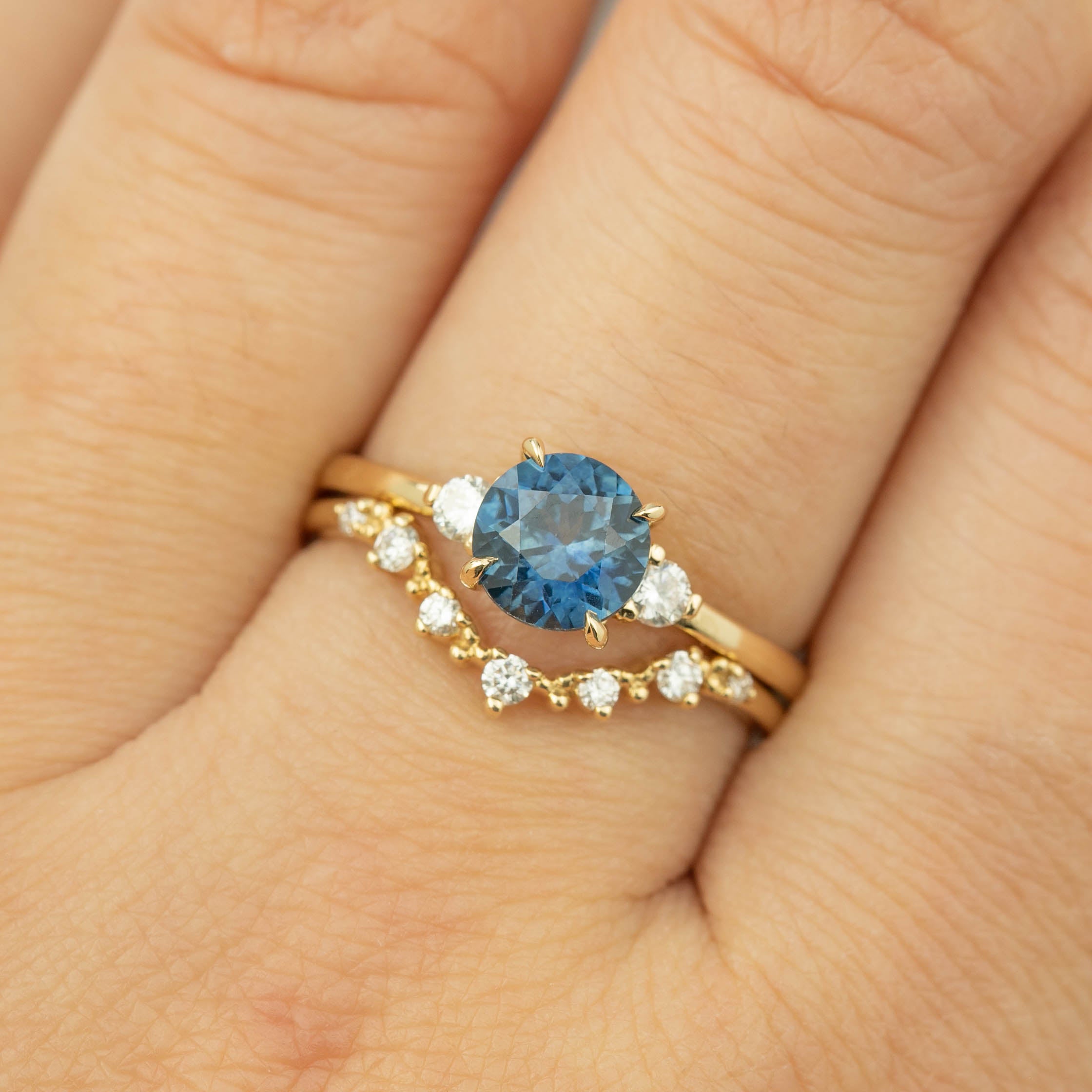 Close-up of a hand wearing a 1.46ct Montana sapphire ring with accent diamonds set in recycled 14k gold band
