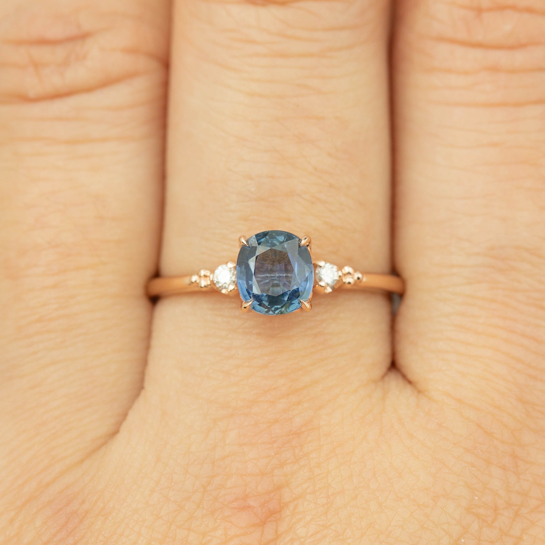 Close-up of Estel Ring featuring 1.24ct blue sapphire and diamond accents set in 14k rose gold band on finger
