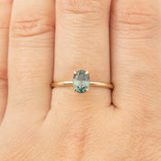 Close-up of Sara Ring with 1.36ct green peacock sapphire set in recycled 14k yellow gold band on finger.