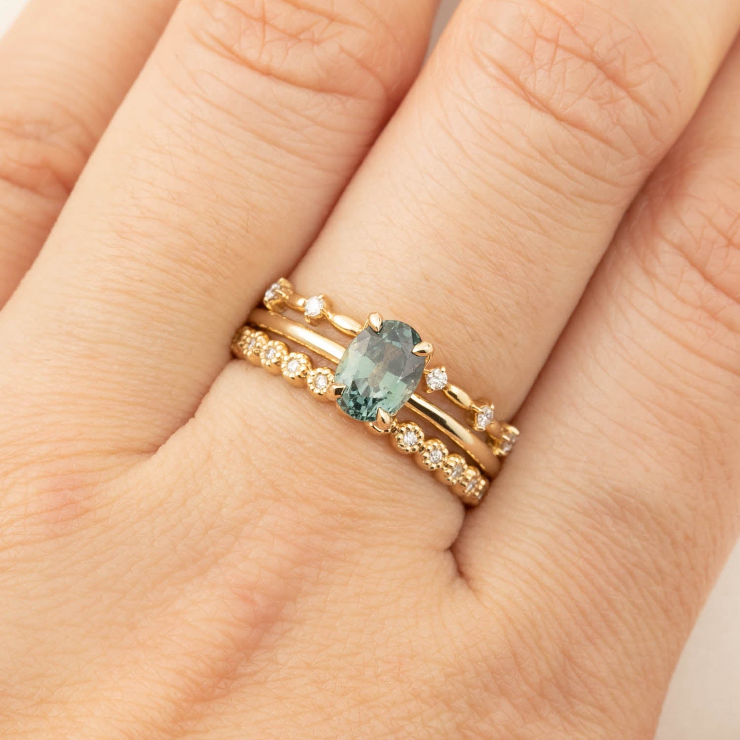 Close-up of hand wearing Sara Ring with 1.36ct green peacock sapphire and 14k yellow gold flower setting band