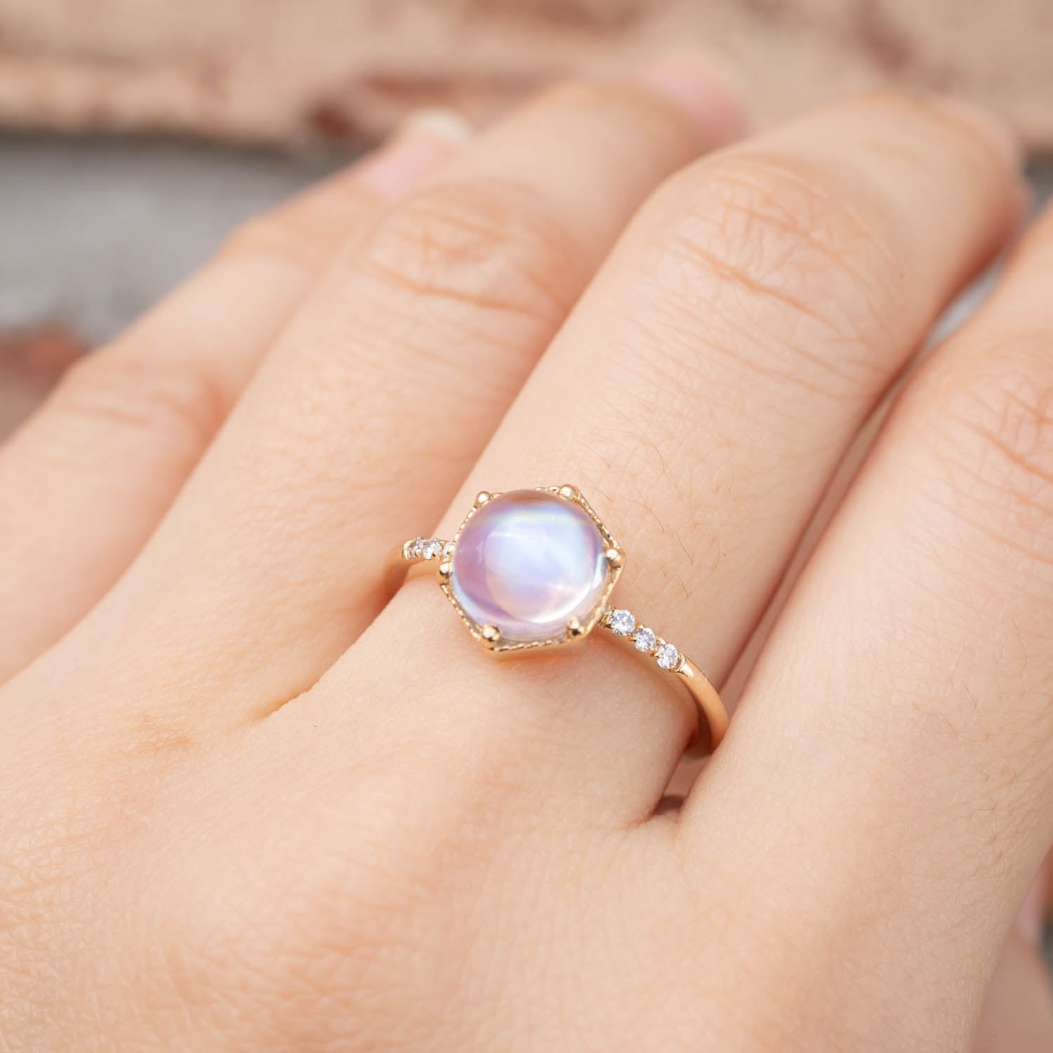 Close-up of hand wearing a handmade 14k gold ring with 1.8ct cabochon rainbow moonstone and white accent diamonds