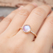 Close-up of hand wearing a handmade 14k gold ring with 1.8ct cabochon rainbow moonstone and white accent diamonds