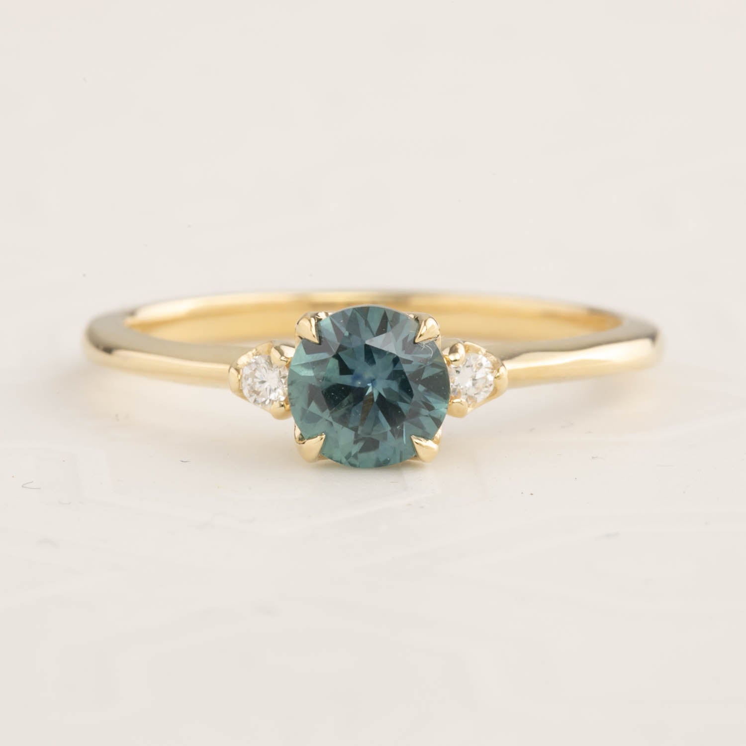 Gold ring with 0.89ct teal blue Montana sapphire and two small white side diamonds on a tapered band