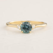 Gold ring with 0.89ct teal blue Montana sapphire and two small white side diamonds on a tapered band