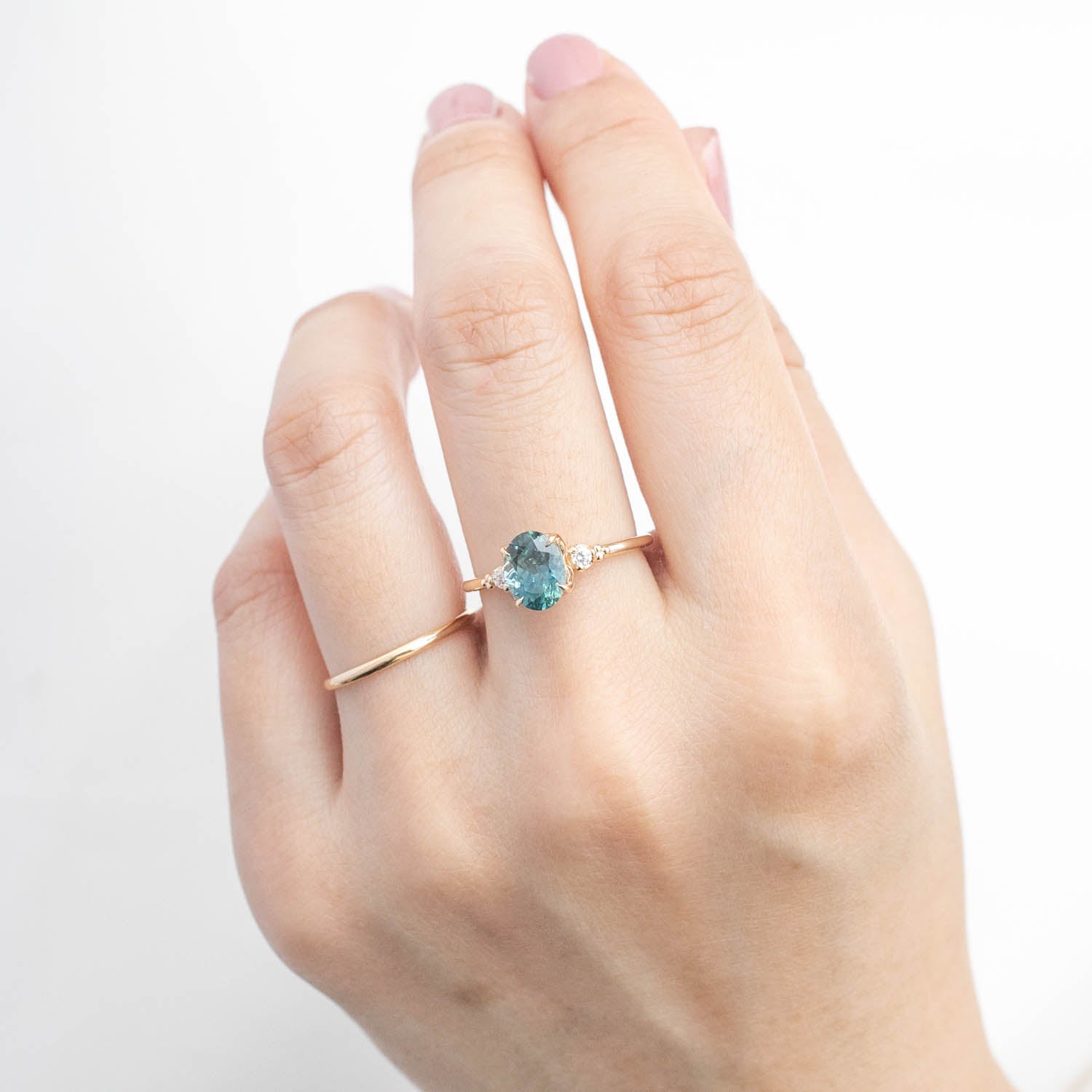 Hand wearing one of a kind 14k yellow gold ring with 1.78ct light blue-green Montana sapphire and accent diamonds