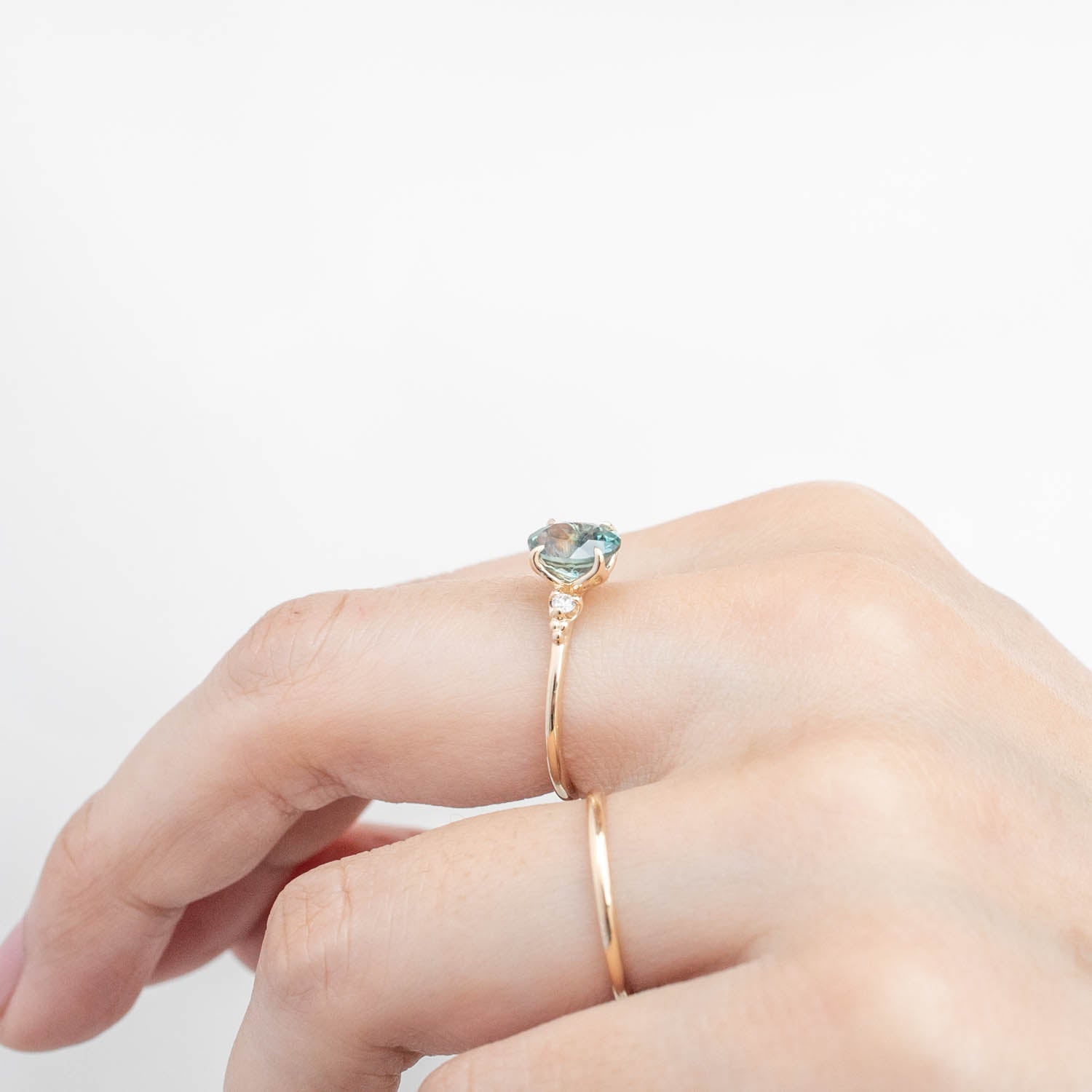 Close-up of hand wearing a 14k yellow gold ring with a 1.78ct light blue-green Montana sapphire and small white diamonds