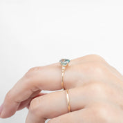 Close-up of hand wearing a 14k yellow gold ring with a 1.78ct light blue-green Montana sapphire and small white diamonds