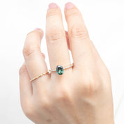 Hand wearing Maria Ring with 1.53ct oval green Queensland sapphire and 14k yellow gold band against white background