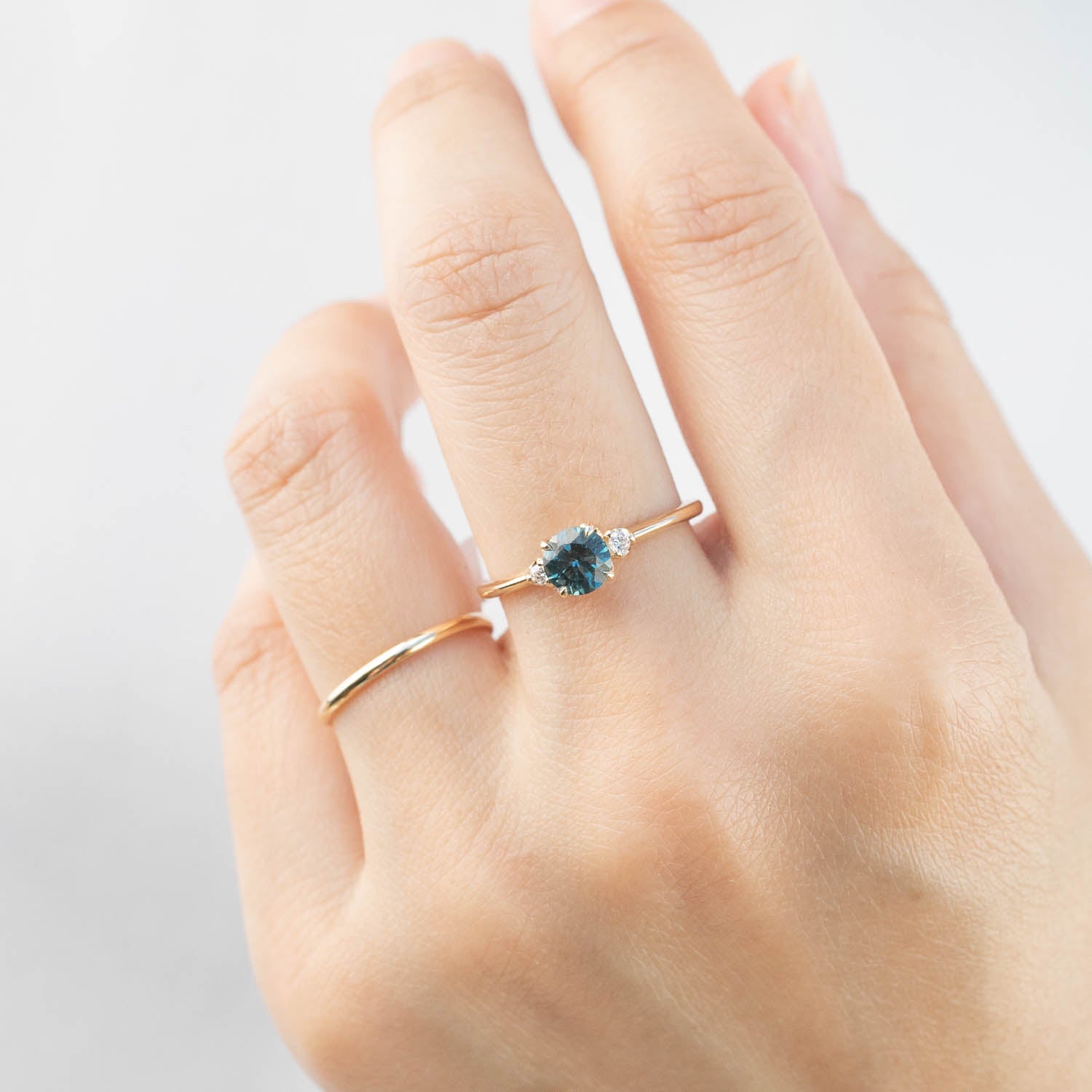 Hand wearing Sofia Ring with 0.89ct teal blue Montana sapphire and white diamond on slender gold band