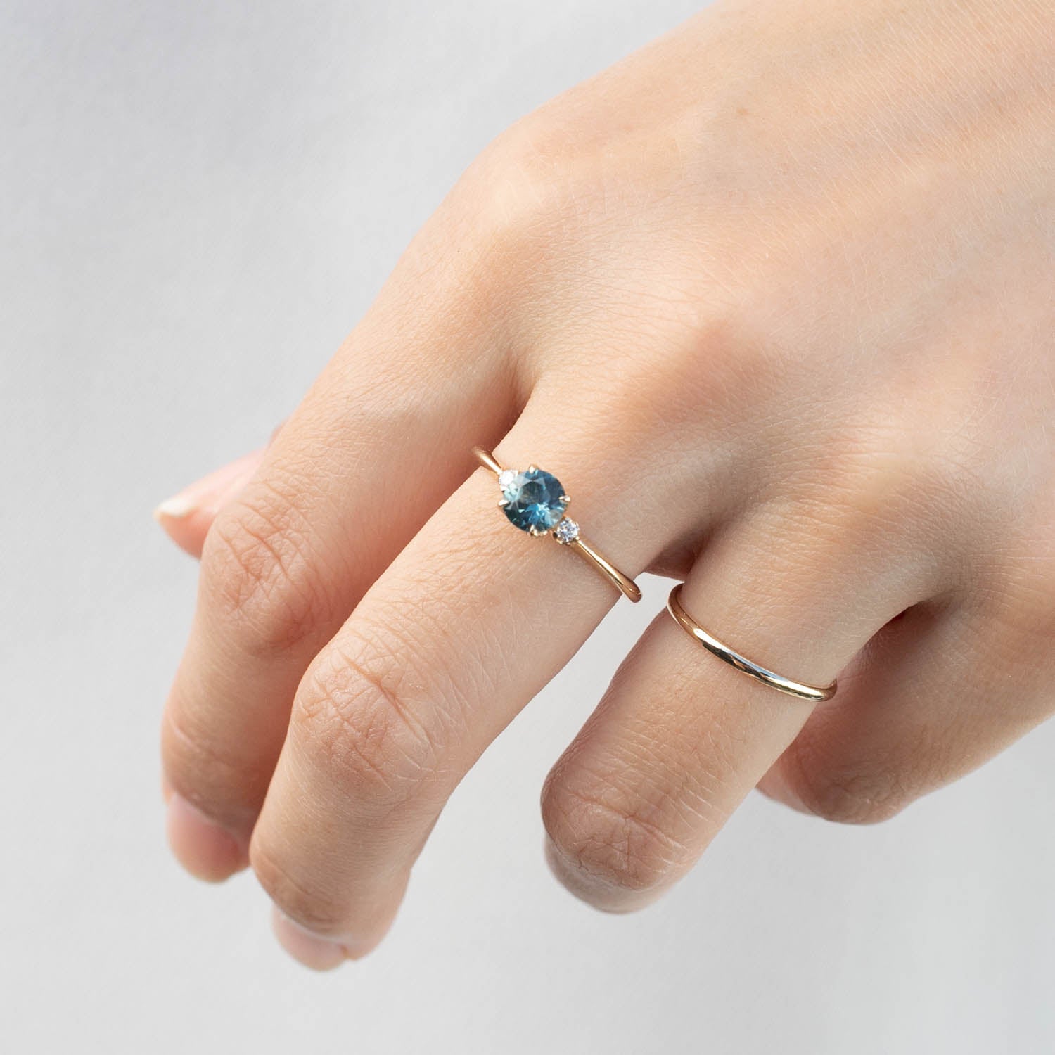 Hand wearing Sofia Ring featuring 0.89ct teal blue Montana sapphire and 0.05ct white diamonds on tapered band