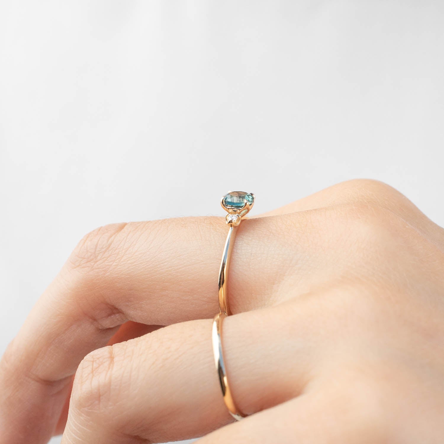 Delicate gold ring with a 0.89ct teal blue Montana sapphire worn on a finger, elegant thin band design.