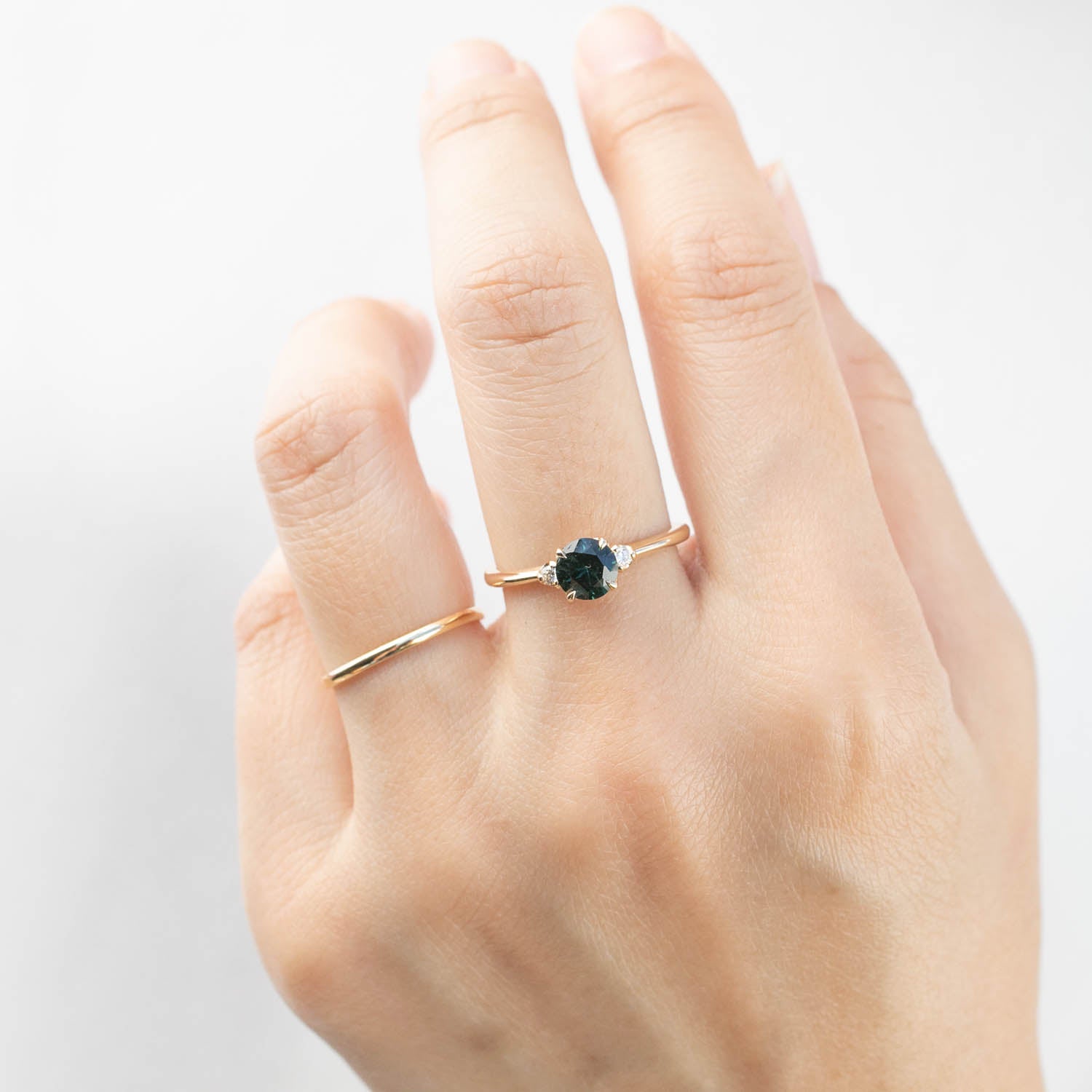Close-up of hand wearing a 14k yellow gold ring with 0.85ct Queensland peacock sapphire and white accent diamonds