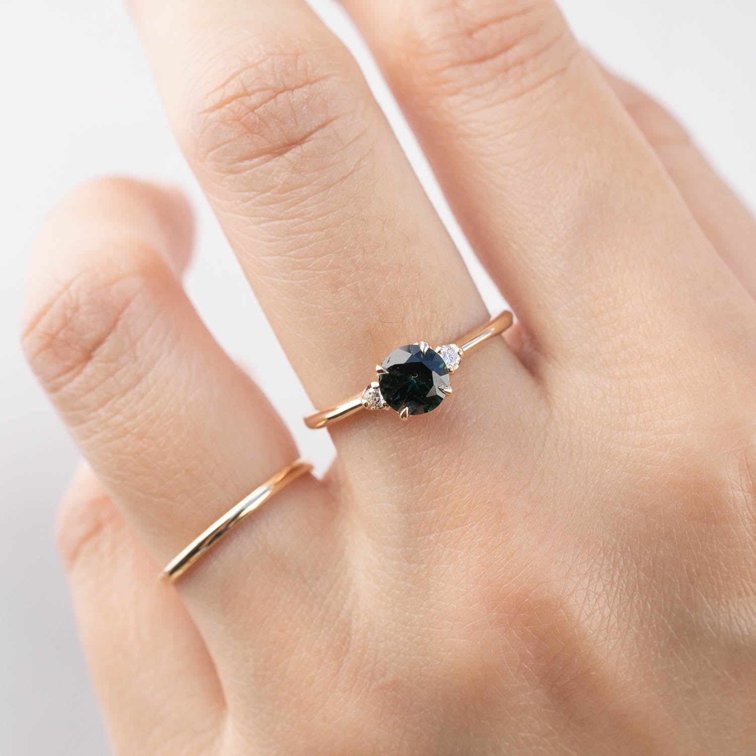 Hand wearing a 14k yellow gold ring with 0.85ct Queensland peacock sapphire and white accent diamonds
