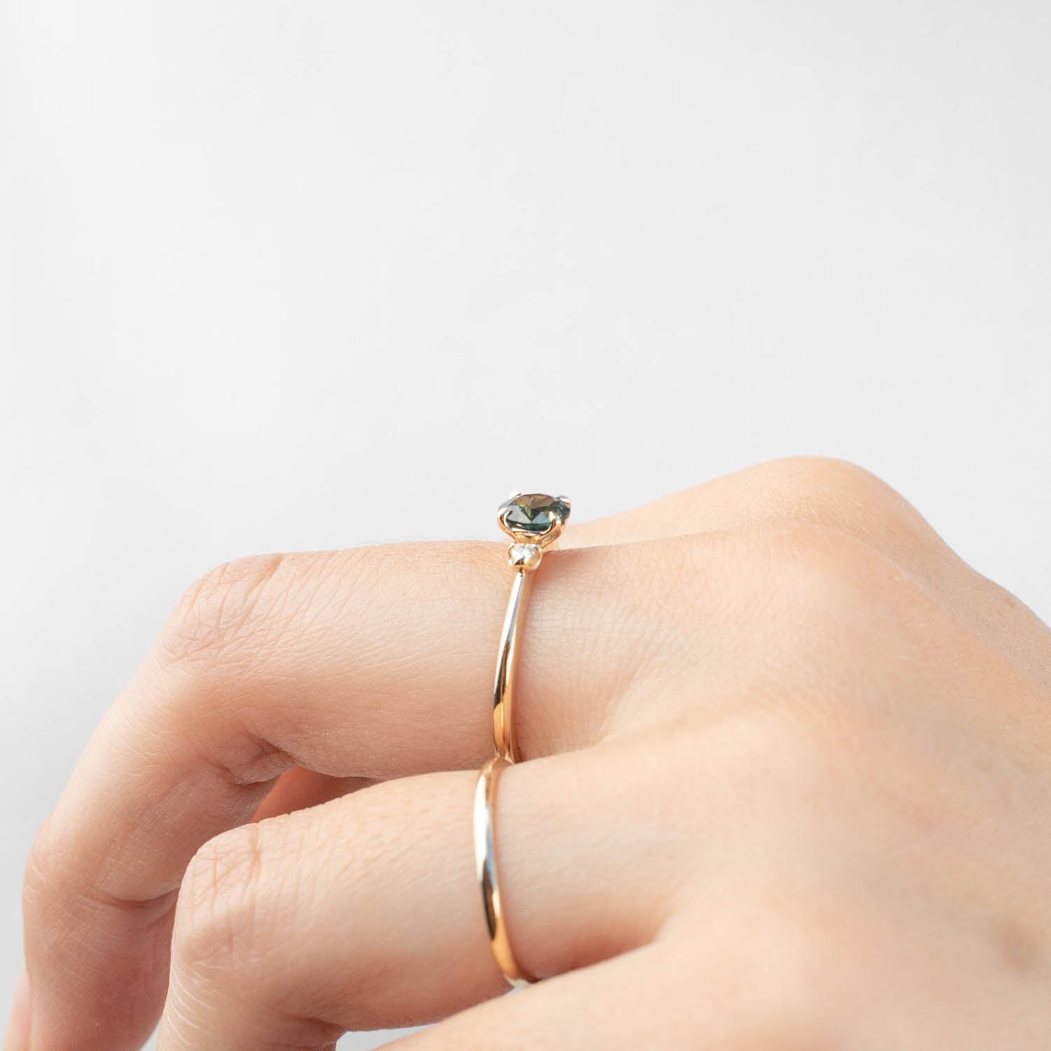 Close-up of a hand wearing a 14k yellow gold Sofia Ring with a 0.85ct Queensland Peacock Sapphire and white diamonds