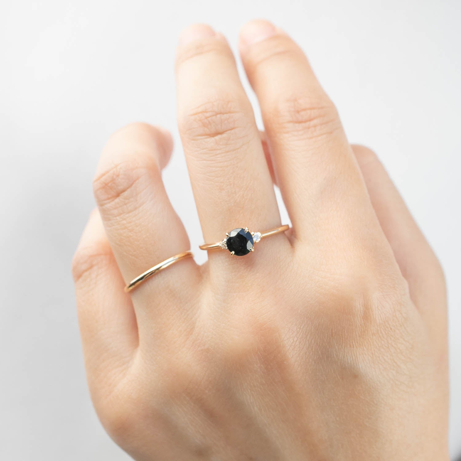 Hand wearing Sofia Ring with 1ct dark peacock sapphire and side white diamonds in 14k yellow gold band