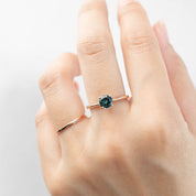Close-up of hand wearing a 0.96ct blue-green Queensland sapphire solitaire ring in 14k rose gold band.