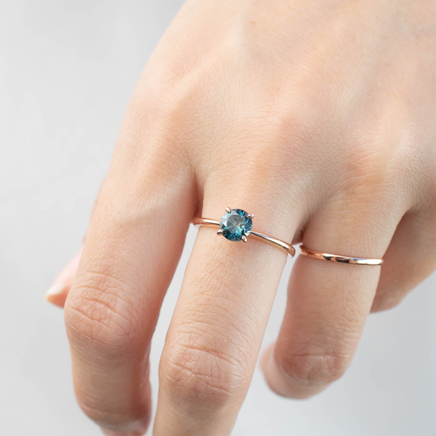 Close-up of a hand wearing a 0.96ct blue-green Queensland sapphire ring in 14k rose gold solitaire setting.