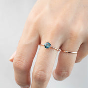 Close-up of a hand wearing a 0.96ct blue-green Queensland sapphire ring in 14k rose gold solitaire setting.
