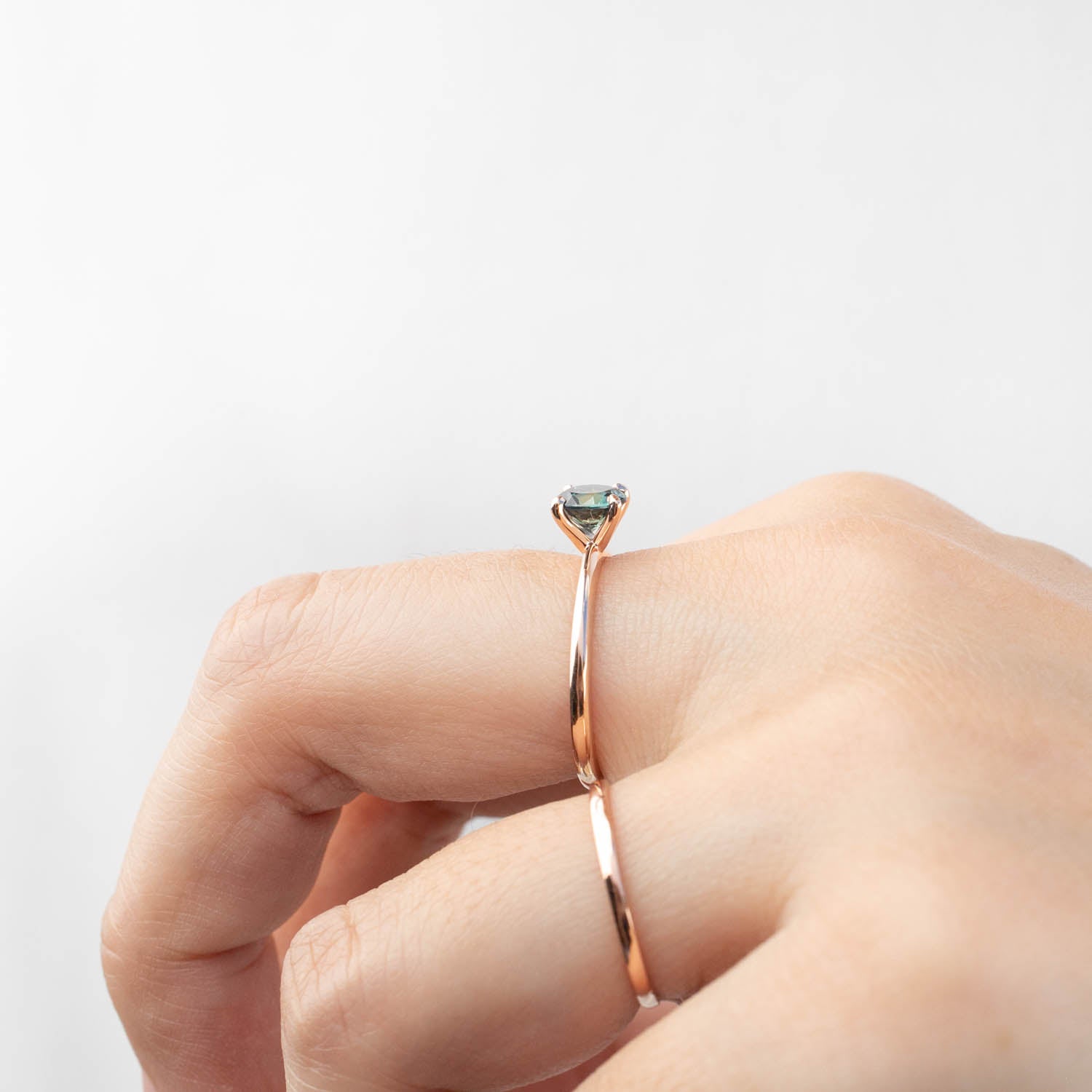 Rose gold solitaire ring featuring a 0.96ct blue-green Queensland sapphire on a tapered band worn on a hand.