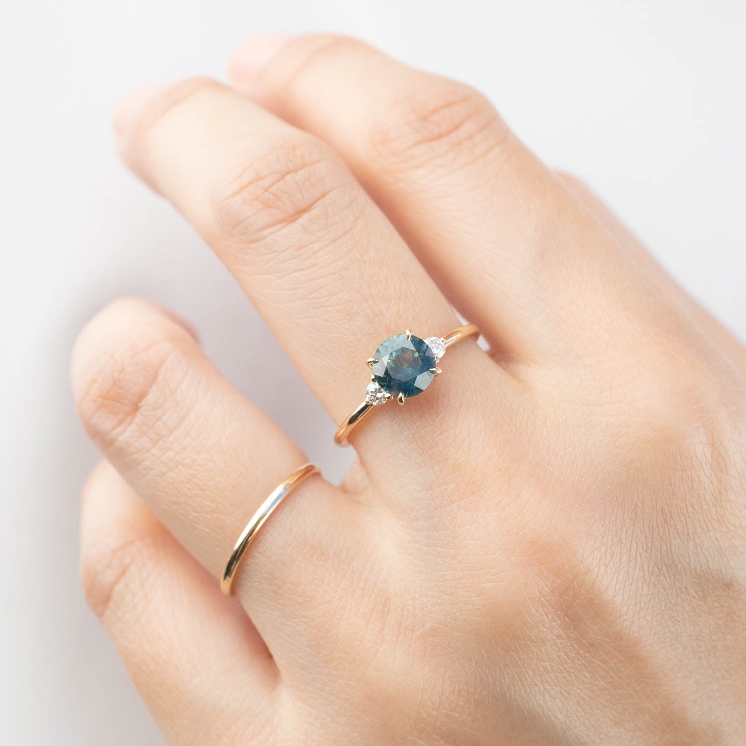 Hand wearing Emilie Ring with 1.31ct blue-green Montana sapphire and diamond accents in 14k gold band