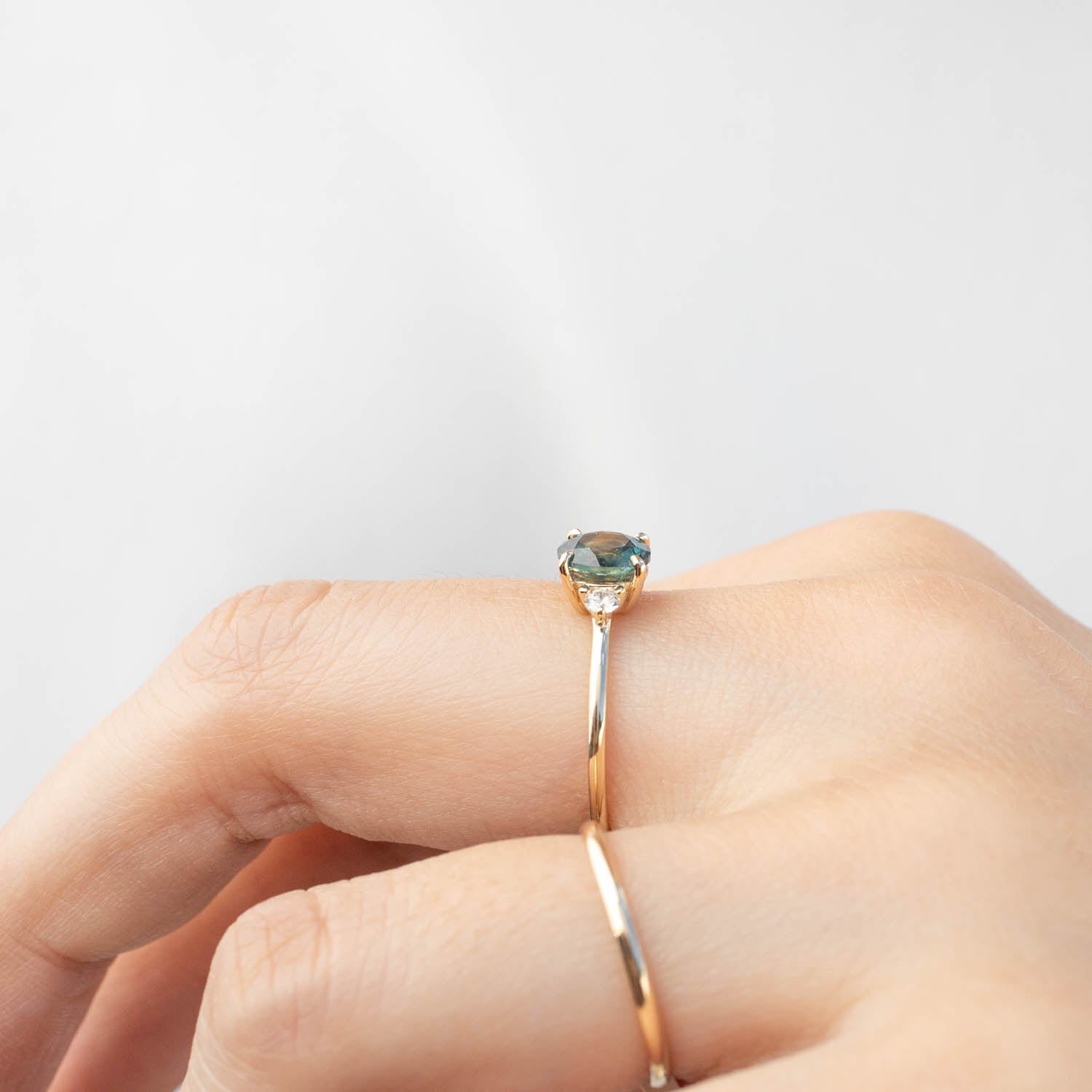 Close-up of a 14k gold ring with a 1.31ct blue-green Montana sapphire on a finger against a white background