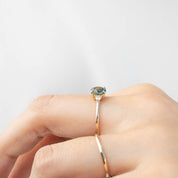 Close-up of a 14k gold ring with a 1.31ct blue-green Montana sapphire on a finger against a white background