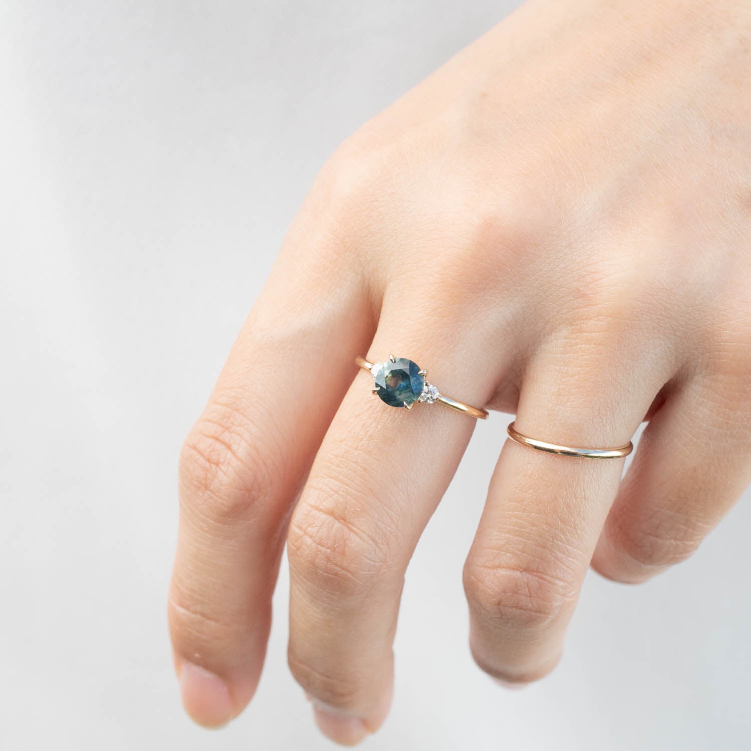 Hand wearing Emilie Ring with 1.31ct blue-green Montana sapphire and diamond accents on a thin recycled 14k gold band