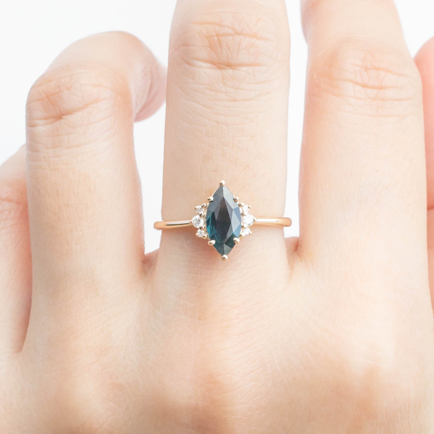 Lena Ring featuring a 0.94ct marquise dark blue green sapphire with white accent diamonds in 14k yellow gold.