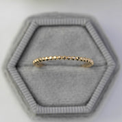 Delicate solid gold bead eternity ring with 1.5mm band width displayed on a gray hexagonal velvet ring box.