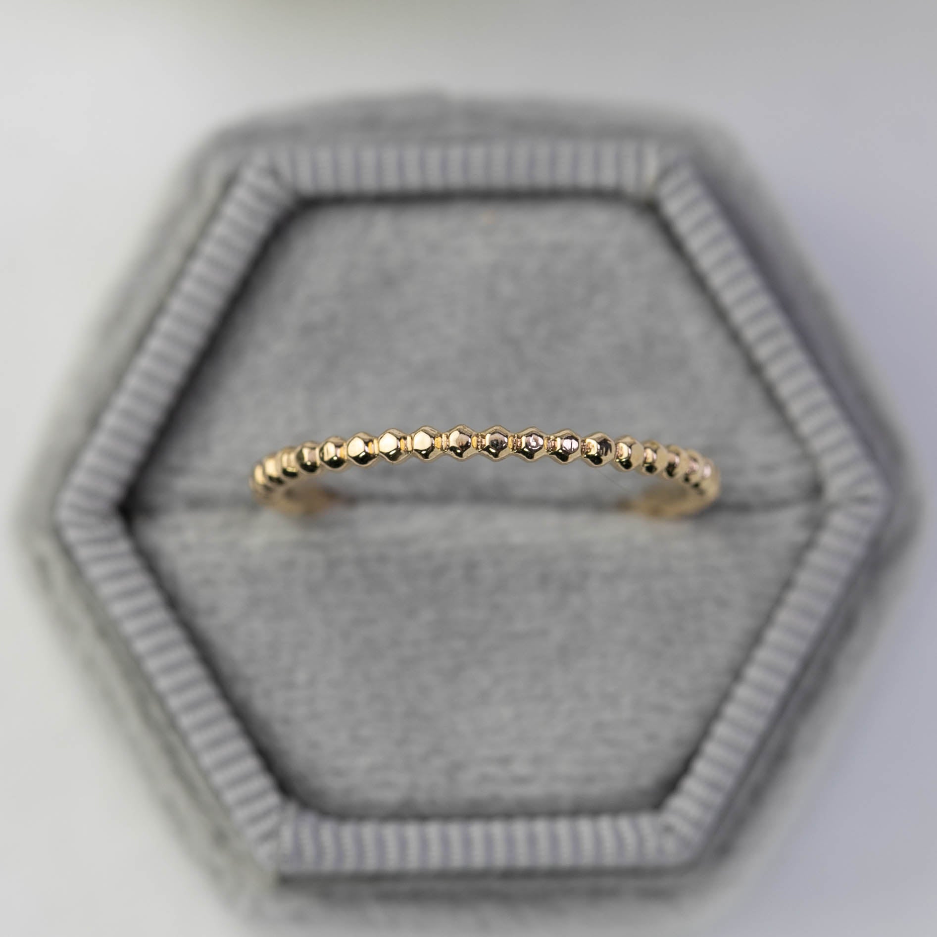 Delicate solid gold bead eternity ring with 1.5mm band width displayed on a gray hexagonal velvet ring box.