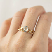 Close-up of a hand wearing a solid gold bead eternity ring with a large oval gemstone centerpiece on a light background