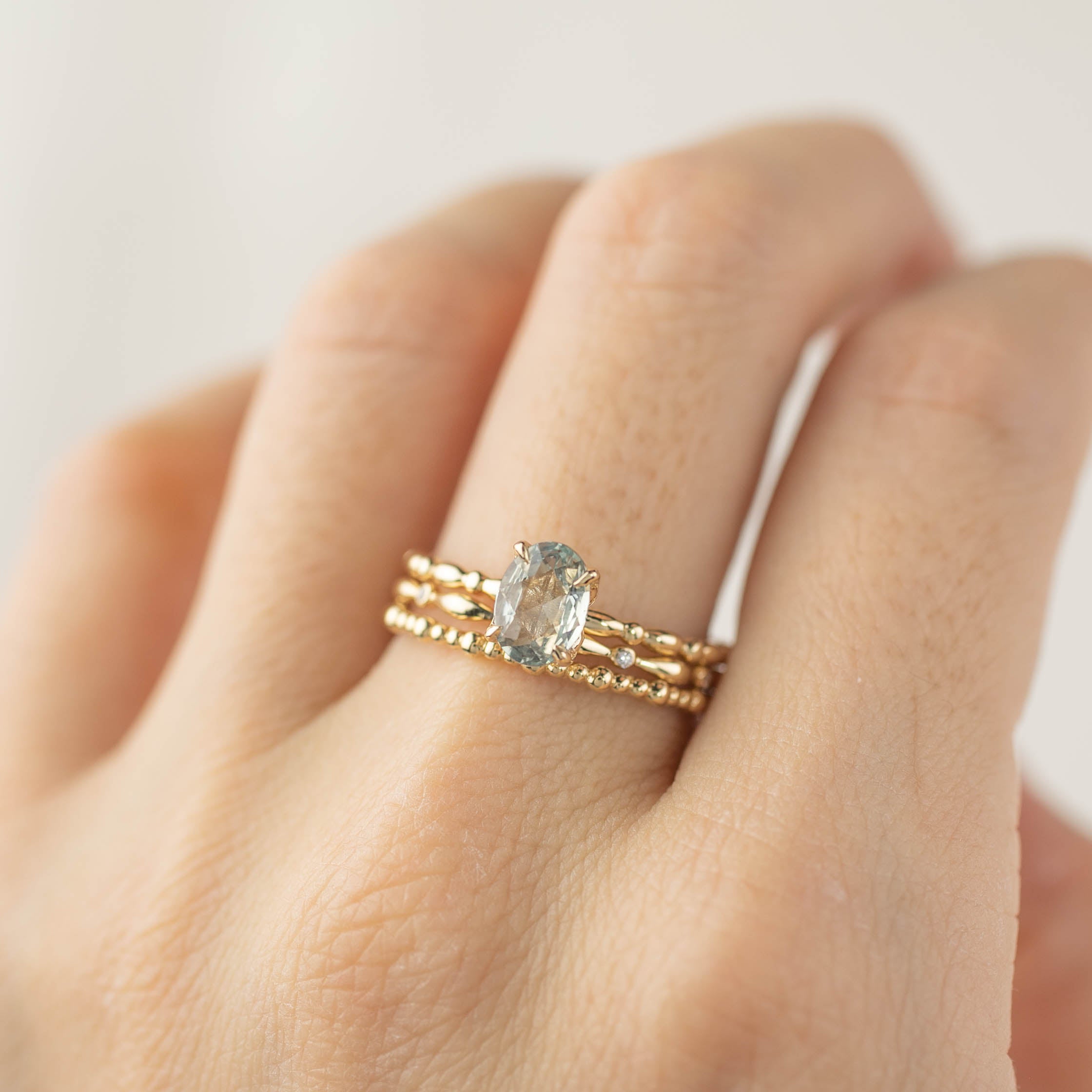 Close-up of a hand wearing a solid gold bead eternity ring with a large oval gemstone centerpiece on a light background