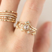 Close-up of a hand wearing stacked delicate gold rings with small white diamonds and geometric designs.