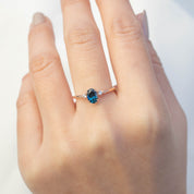Hand wearing Estel Ring with 0.83ct teal blue sapphire and white accent diamonds in 14k rose gold band