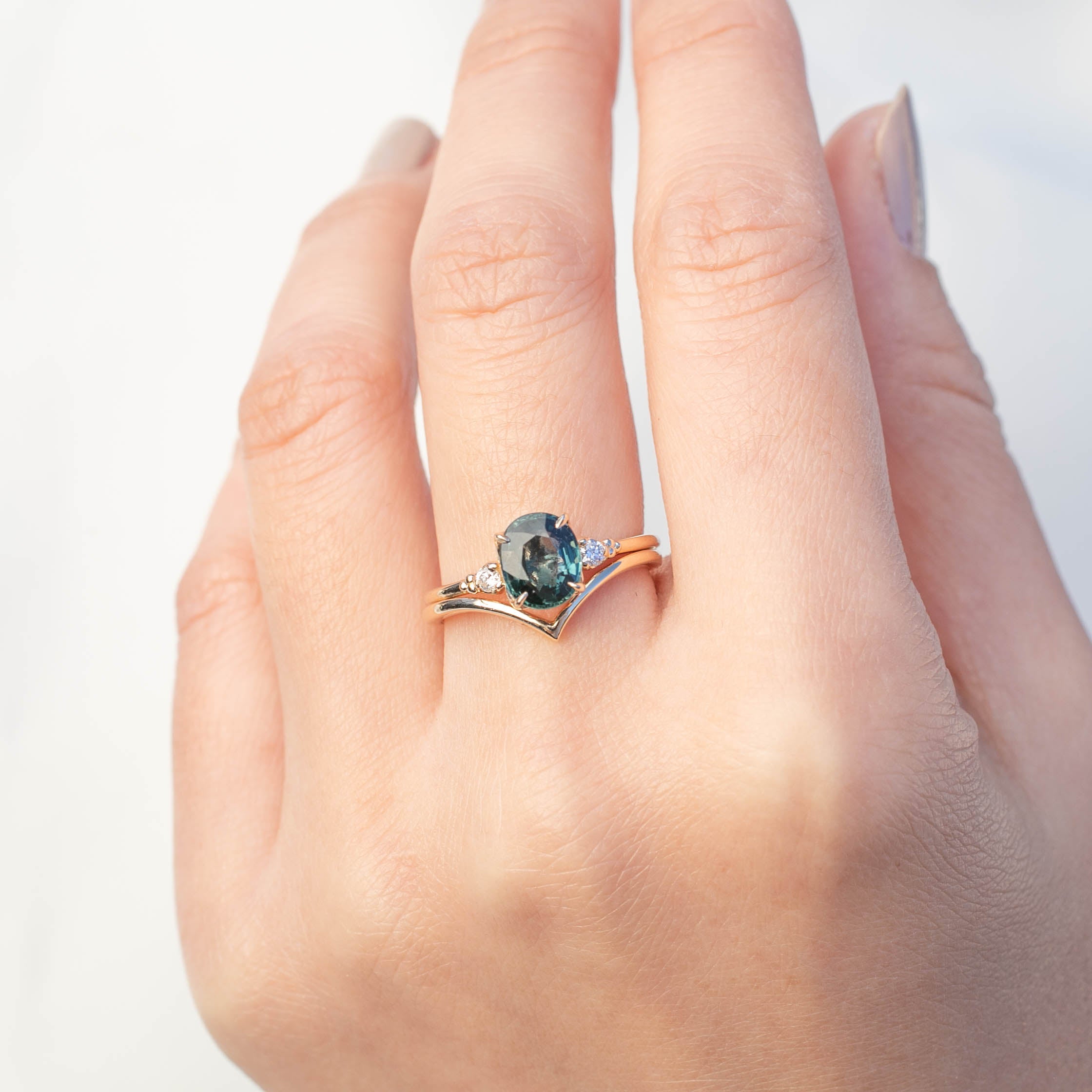Hand wearing Estel Ring featuring 1.56ct teal blue Montana sapphire with white diamond accents in 14k gold band.