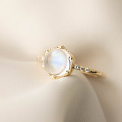 14k yellow gold Grace Ring with 1.8ct cabochon rainbow moonstone and white accent diamonds on satin background