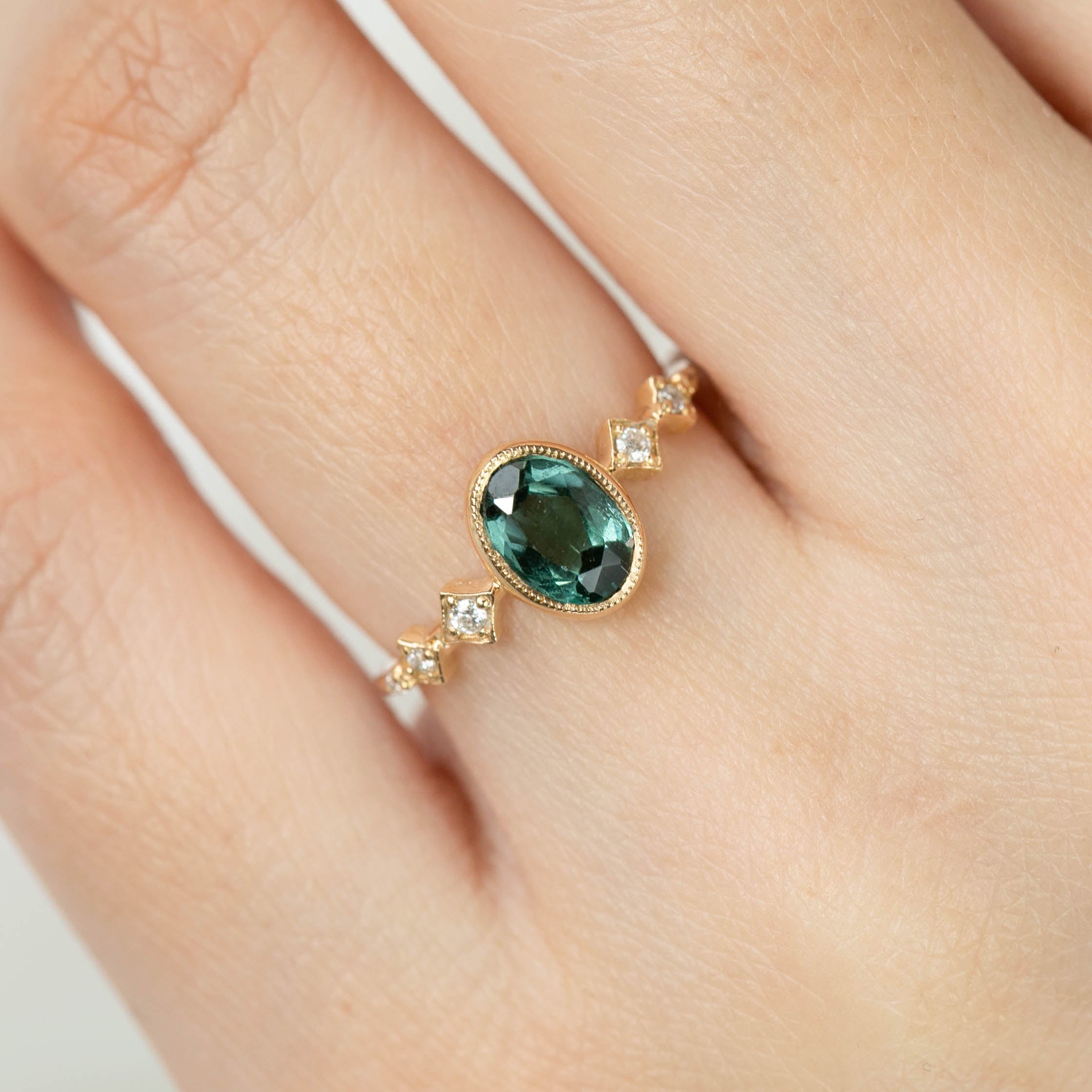 Hand wearing 14k yellow gold Celeste Ring with 1.02ct green tourmaline and white accent diamonds in bezel setting