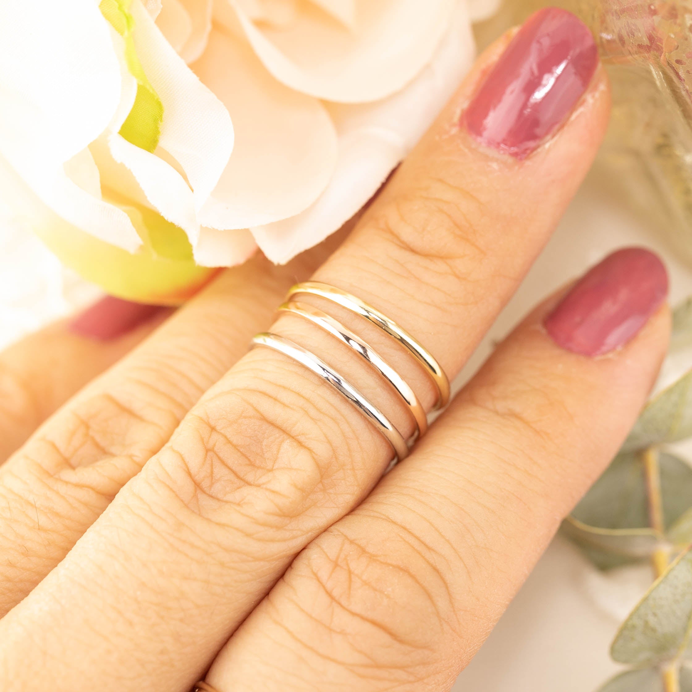 Hand wearing three Half-Round Straight Band (1.3mm) rings in gold and silver, handmade and ethically sourced by Envero Jewelry.