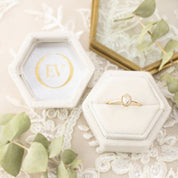 White velvet hexagon ring box with gold foil Envero Jewelry logo and delicate gold ring inside on lace background
