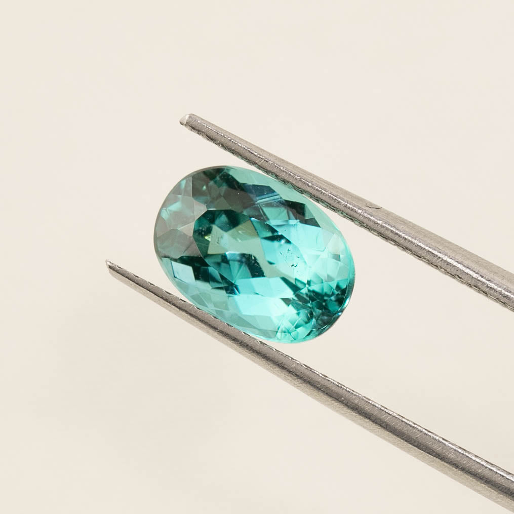 1.76ct oval cut green tourmaline gemstone held by tweezers on a neutral background