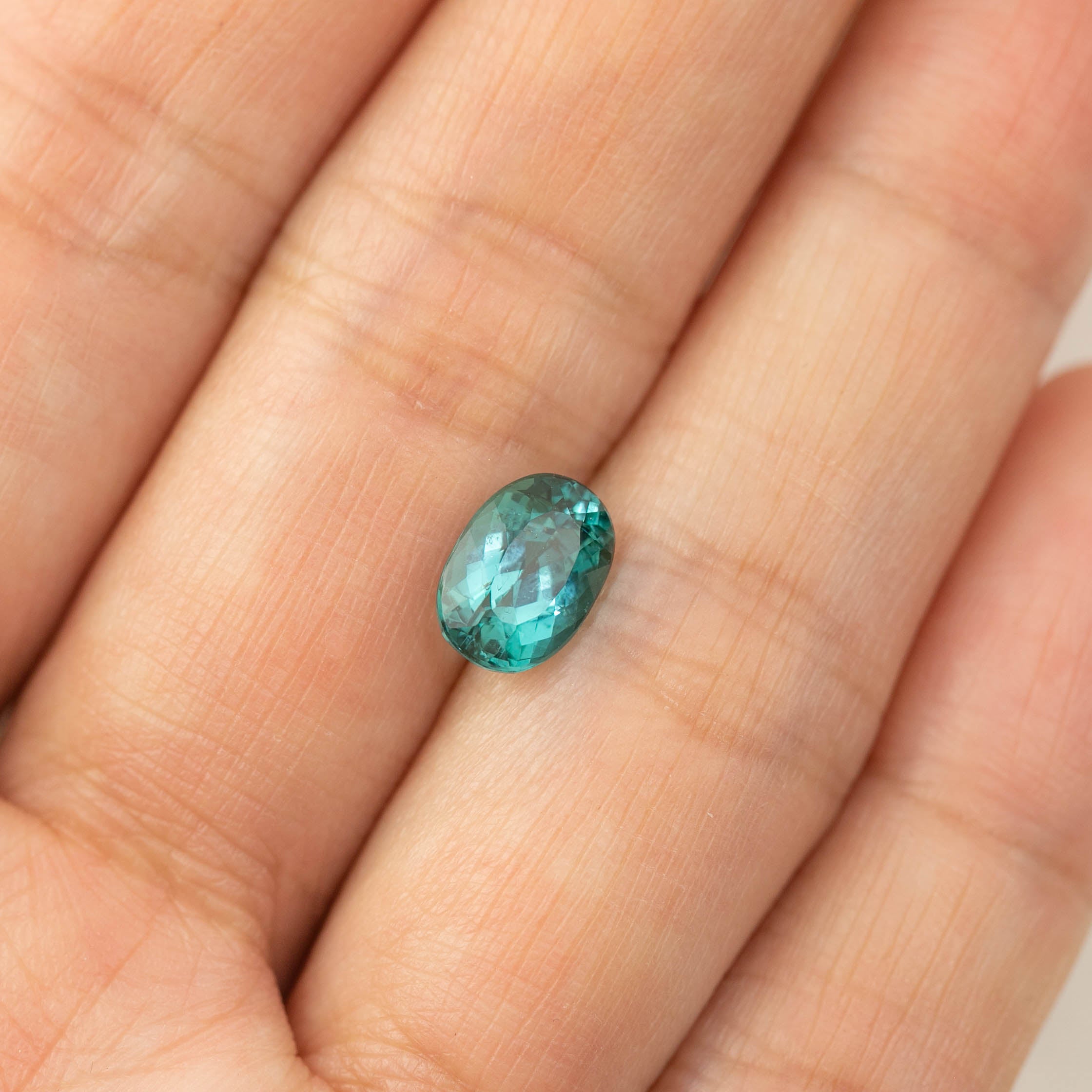 Oval cut 1.76ct green tourmaline gemstone from Namibia held on a fingertip showing size and color details