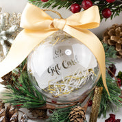 Clear Christmas ornament with Envero gift card inside, decorated with gold bow and holiday greenery background.