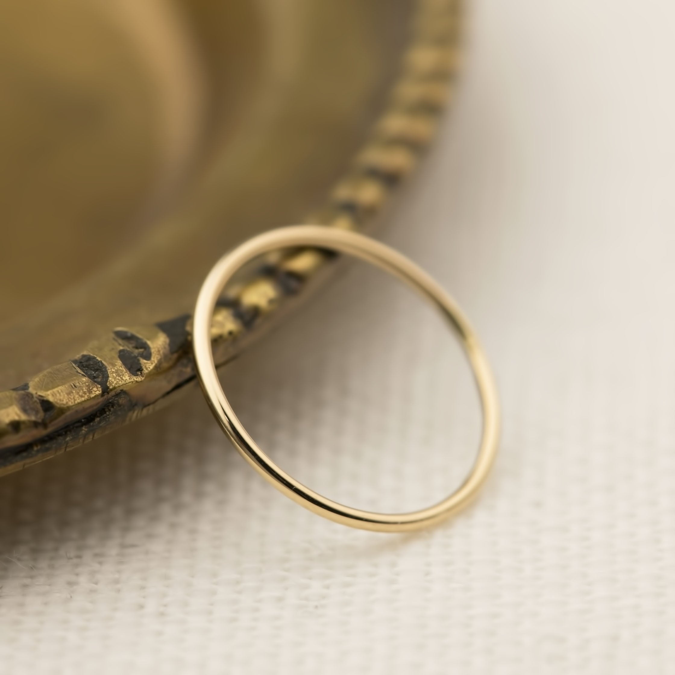 Handmade Half-Round Straight Band (1.3mm) resting on a textured brass dish, from Envero Jewelry on Etsy.
