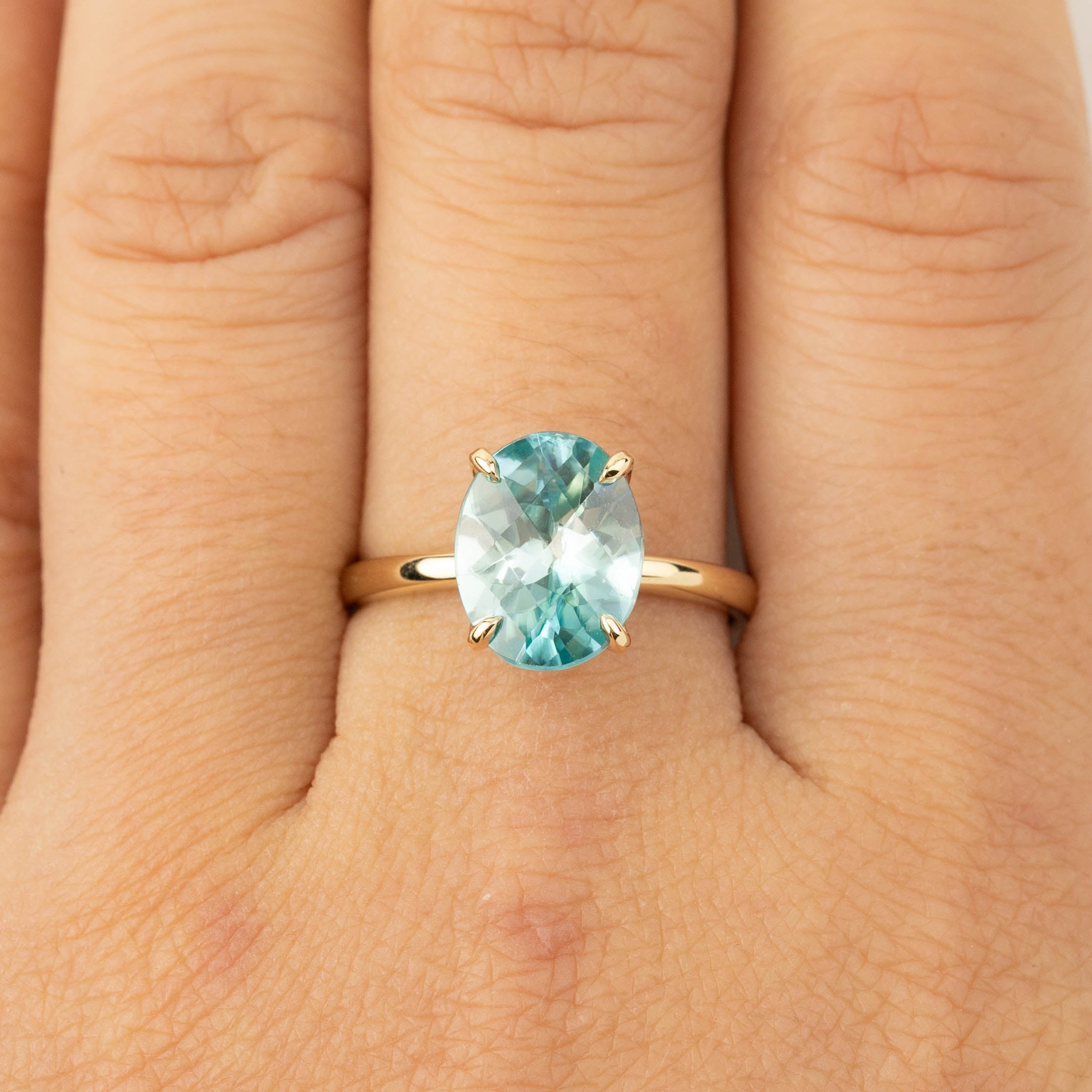 Close-up of Sara Ring with 4ct blue zircon checkerboard cut set on 14k yellow gold band on finger.