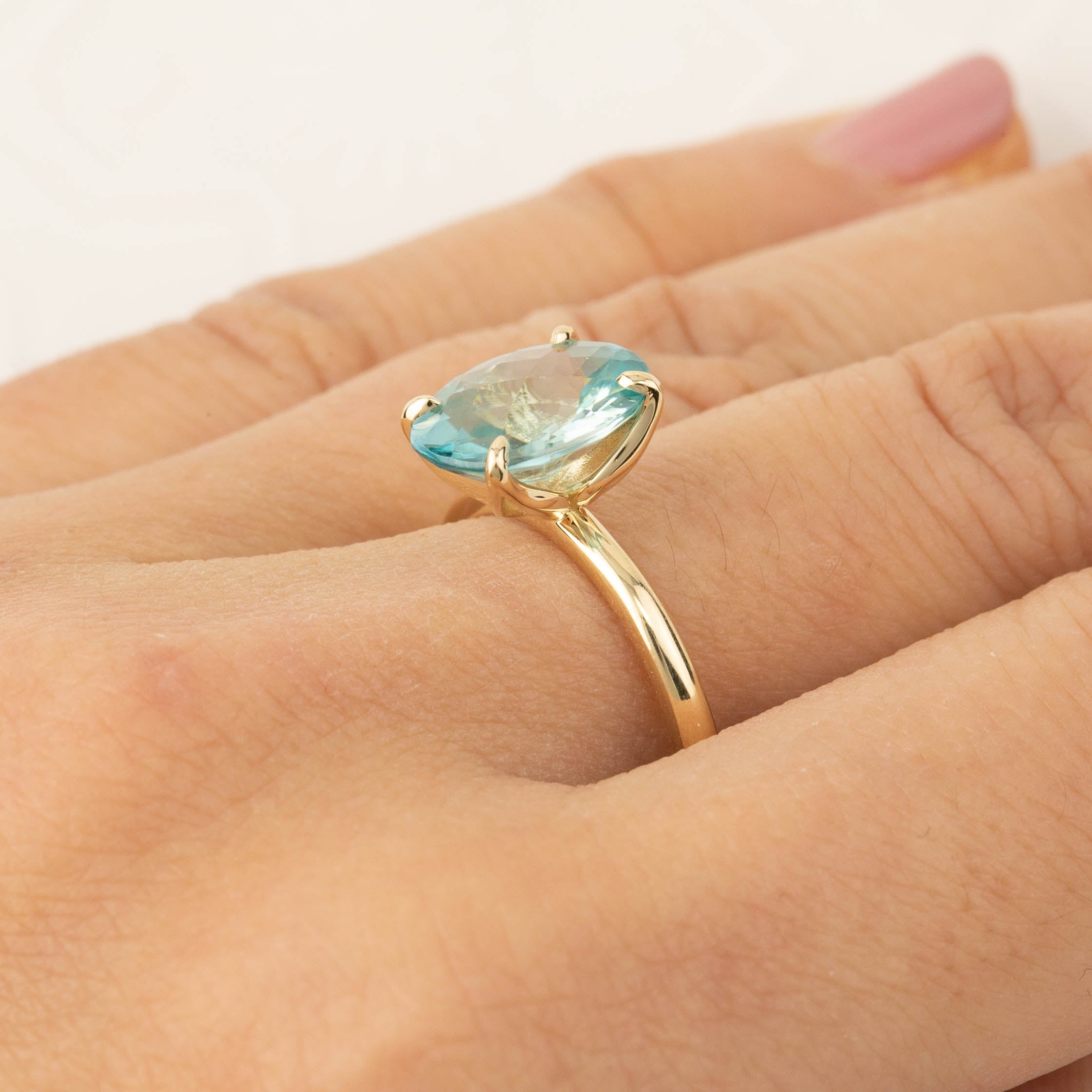 Close-up of a hand wearing a Sara Ring with a 4ct blue zircon checkerboard cut in 14k yellow gold band