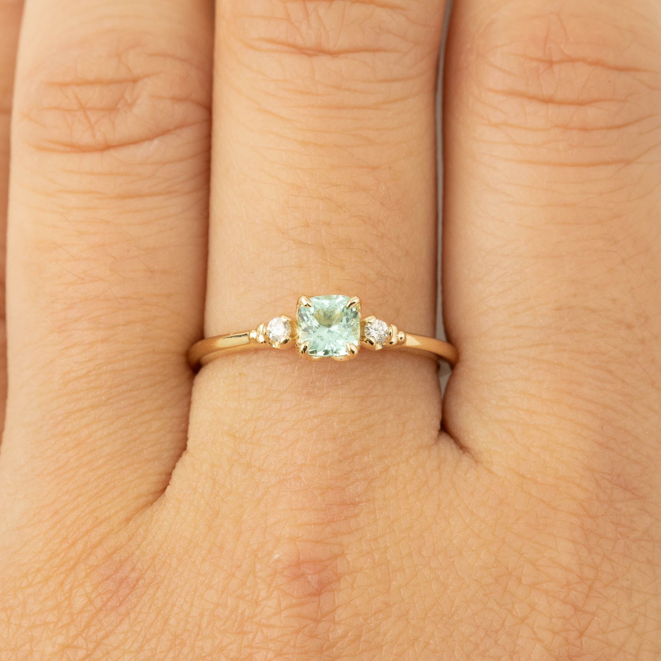 Gold ring with 4.5mm cushion cut natural mint tourmaline and two small brilliant cut diamonds on finger