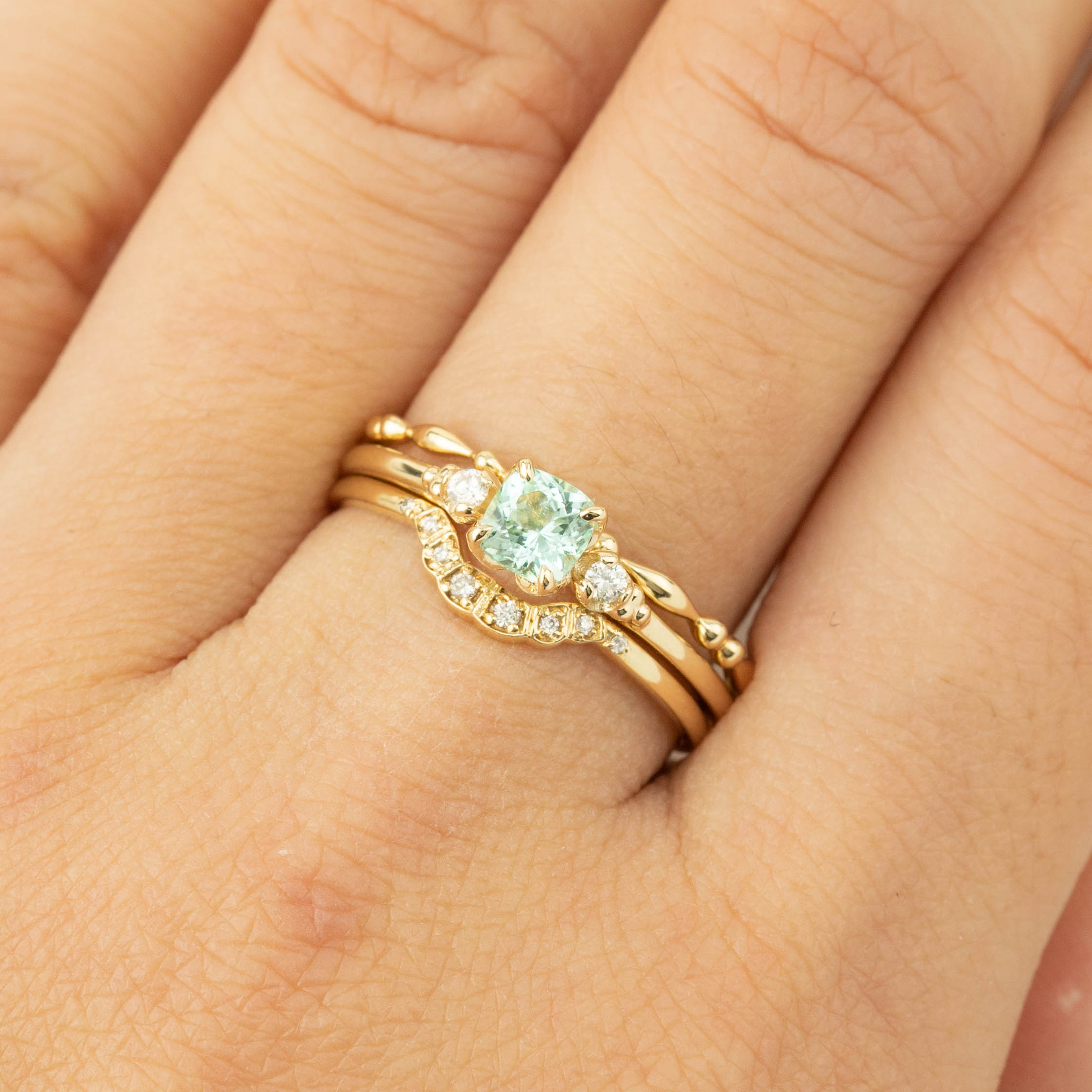 Close-up of hand wearing Estel Ring with 4.5mm cushion cut natural mint tourmaline and diamond accents on gold band