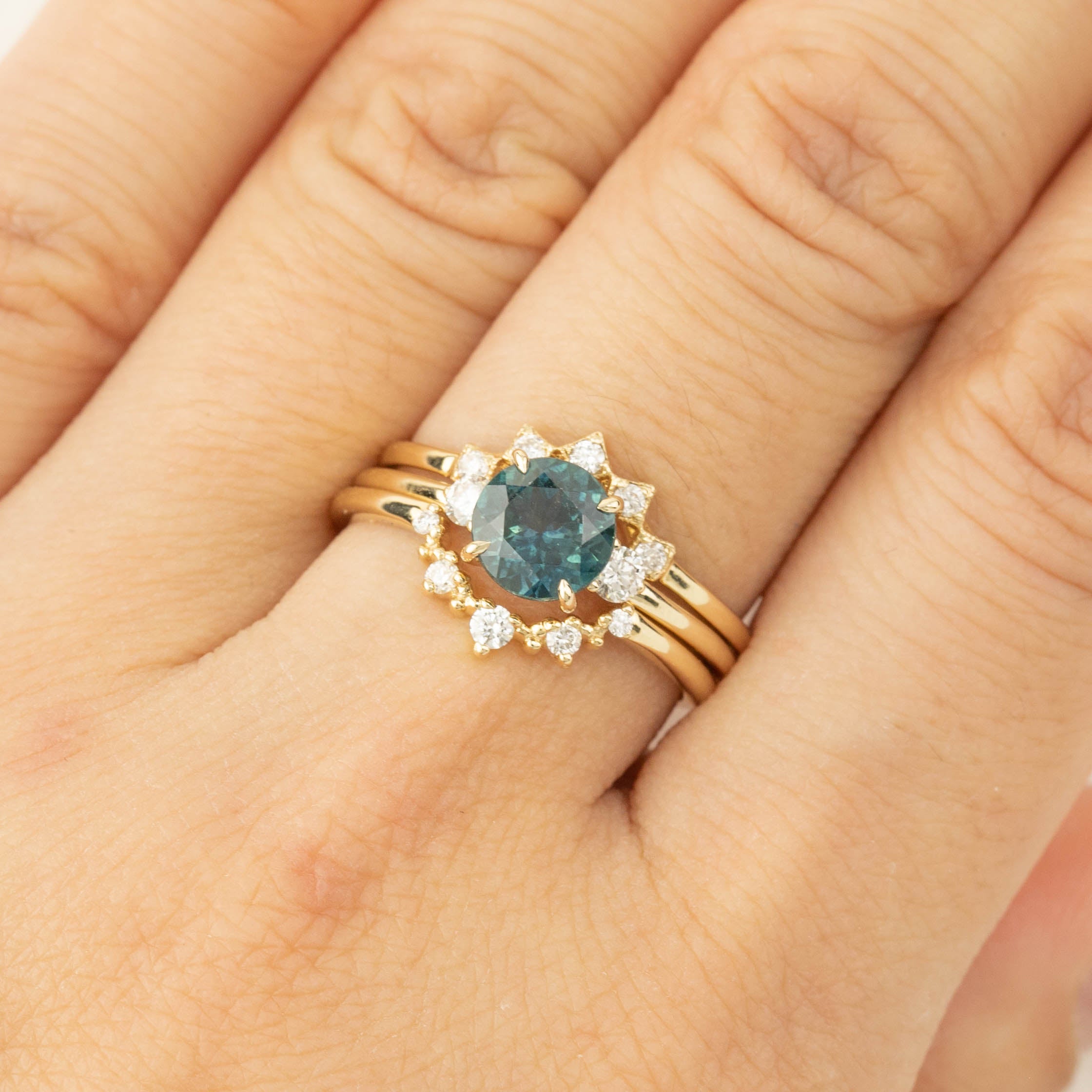Three stone ring with 1.48ct green Montana sapphire and white diamond accents set in 14k gold on finger.
